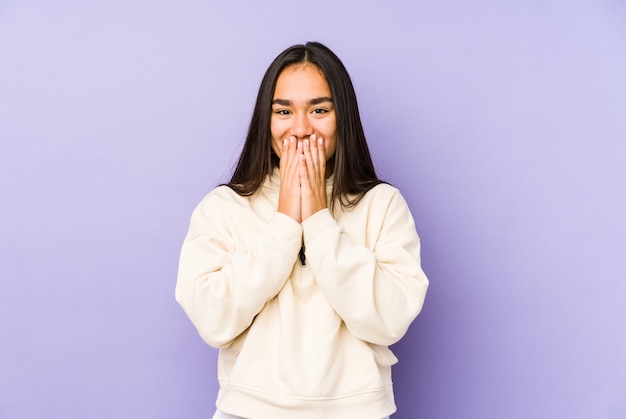 Mulher jovem isolada em um fundo roxo, rindo de algo, cobrindo a boca com as mãos.