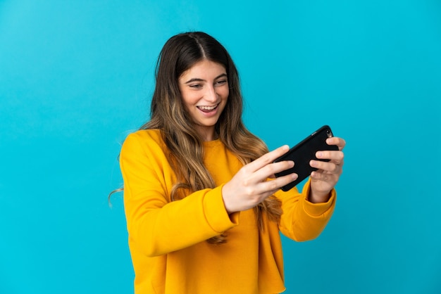 Mulher jovem isolada na parede azul brincando com o celular