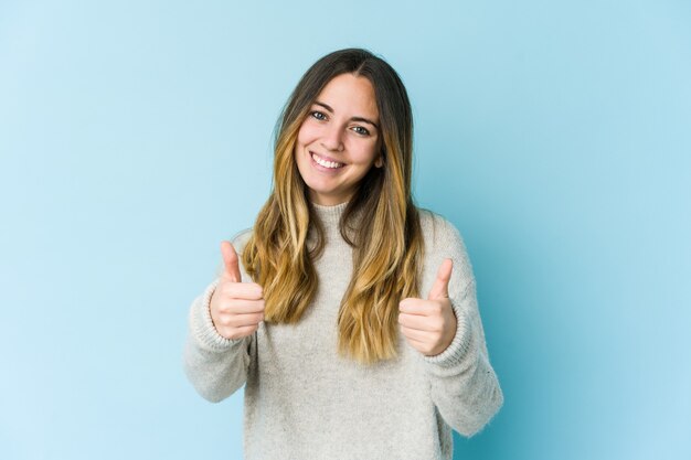 Mulher jovem isolada na parede azul sorrindo e levantando o polegar