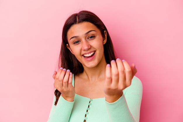 Mulher jovem isolada na parede rosa apontando com o dedo para você como se fosse um convite para se aproximar