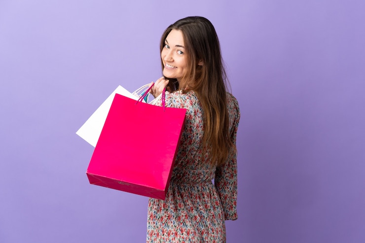 Foto mulher jovem isolada na parede roxa segurando sacolas de compras e sorrindo