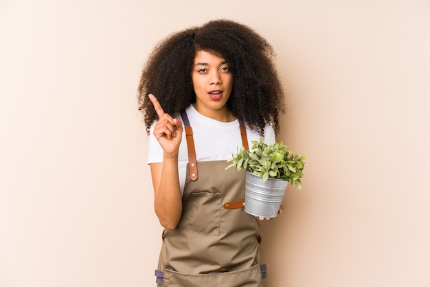 Mulher jovem jardineiro afro segurando uma planta isolada, tendo uma ideia, o conceito de inspiração.