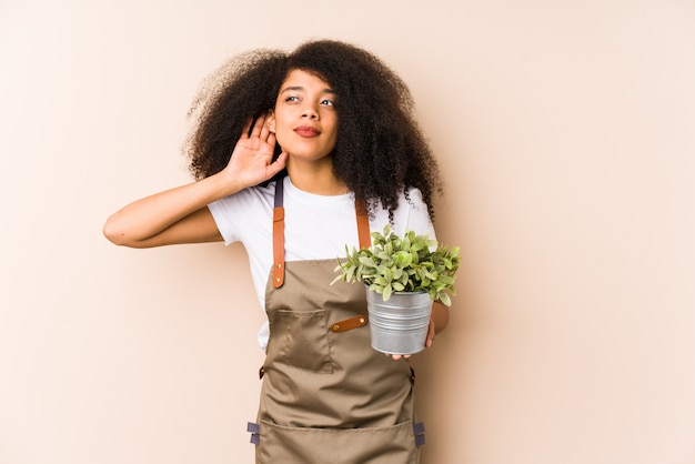 Mulher jovem jardineiro afro segurando uma planta tentando ouvir uma fofoca.