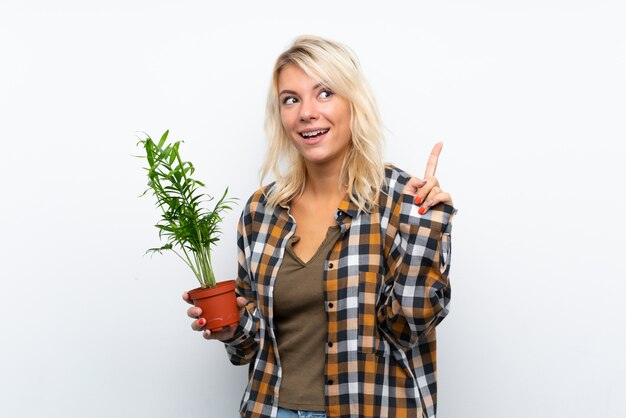 Mulher jovem jardineiro loira segurando uma planta com a intenção de realizar a solução enquanto levanta um dedo