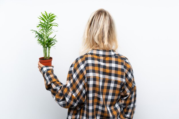 Mulher jovem jardineiro loira segurando uma planta em posição traseira