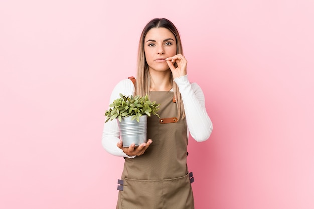 Mulher jovem jardineiro segurando uma planta com os dedos nos lábios, mantendo um segredo.