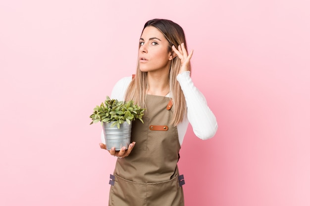 Mulher jovem jardineiro segurando uma planta tentando ouvir uma fofoca.