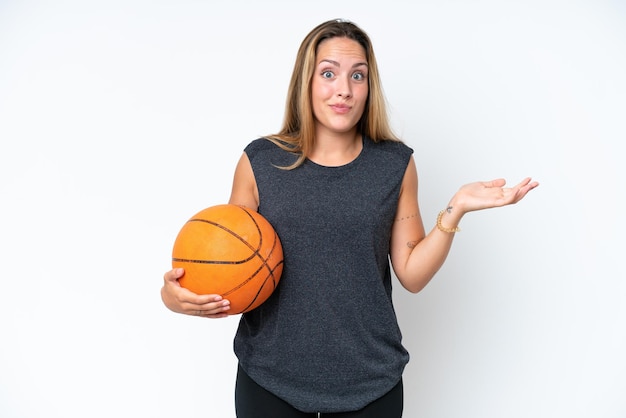 Mulher jovem jogador caucasiano de basquete isolada no fundo branco com dúvidas ao levantar as mãos