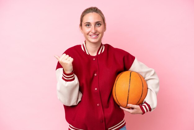 Foto mulher jovem jogador caucasiano de basquete isolada no fundo rosa, apontando para o lado para apresentar um produto