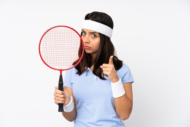 Mulher jovem jogador de badminton sobre branco isolado frustrada e apontando para a frente