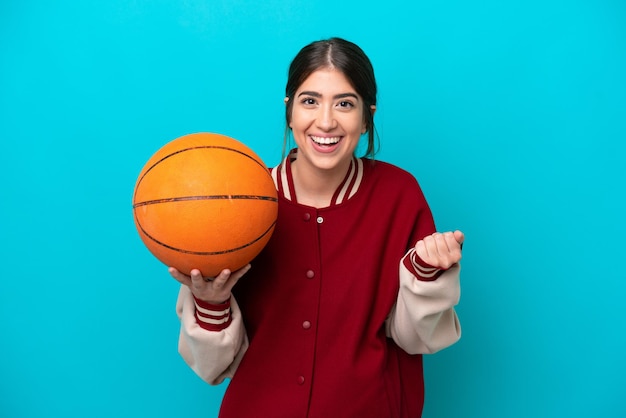 Mulher jovem jogador de basquete caucasiano isolada em fundo azul comemorando uma vitória na posição de vencedor