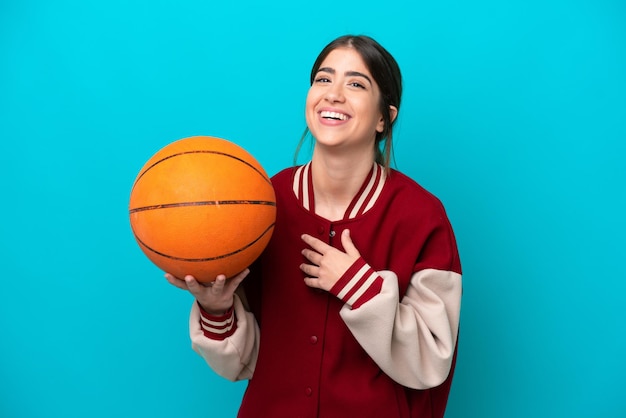 Mulher jovem jogador de basquete caucasiano isolada em fundo azul sorrindo muito