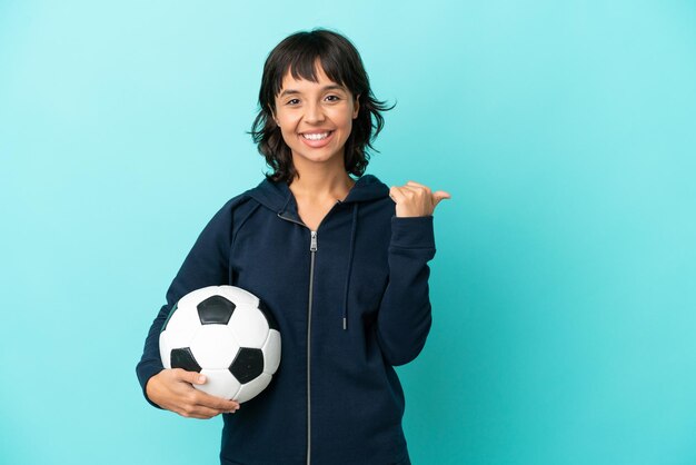 Mulher jovem jogador de futebol de raça mista isolada em fundo azul, apontando para o lado para apresentar um produto