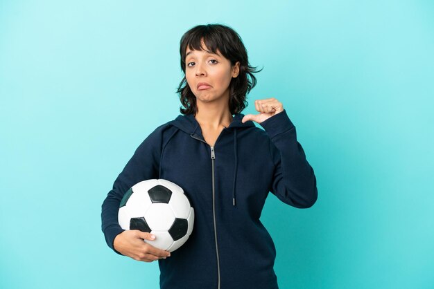 Mulher jovem jogador de futebol de raça mista isolada em fundo azul orgulhosa e satisfeita