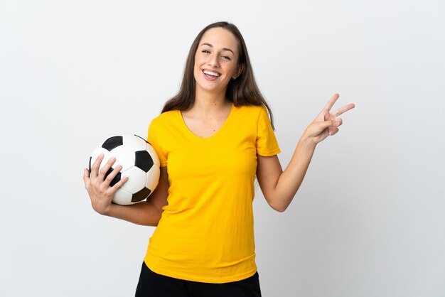 Mulher jovem jogador de futebol em branco isolado sorrindo e mostrando sinal de vitória