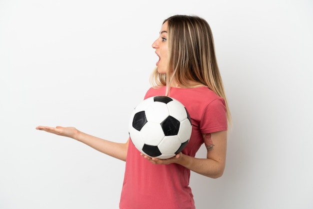 Mulher jovem jogador de futebol em uma parede branca isolada com expressão de surpresa enquanto olha para o lado