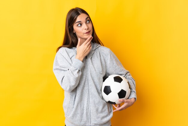 Mulher jovem jogador de futebol isolada em amarelo olhando para cima enquanto sorri