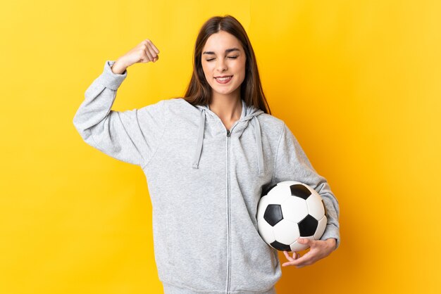 Mulher jovem jogador de futebol isolada em fundo amarelo fazendo um gesto forte