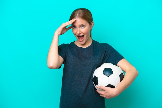 Mulher jovem jogador de futebol isolada em fundo azul com expressão de surpresa