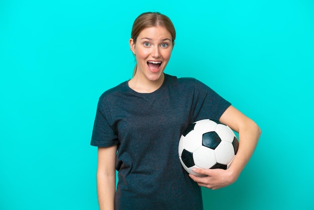 Mulher jovem jogador de futebol isolada em fundo azul com expressão facial de surpresa