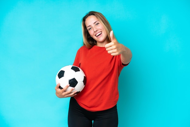 Mulher jovem jogador de futebol isolada em fundo azul com polegares para cima porque algo bom aconteceu