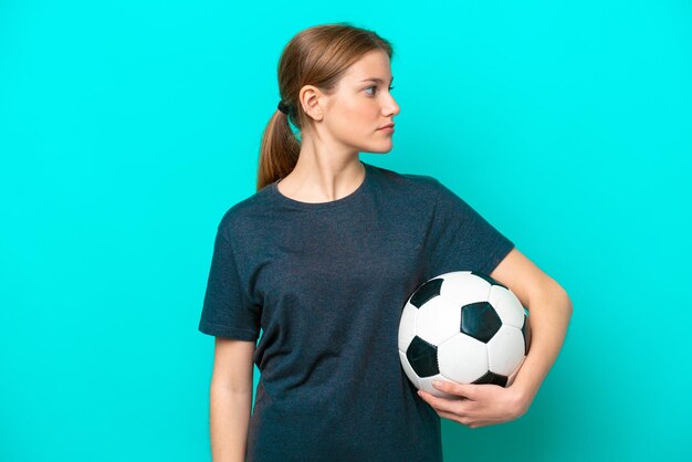 Mulher jovem jogador de futebol isolada em fundo azul, olhando para o lado
