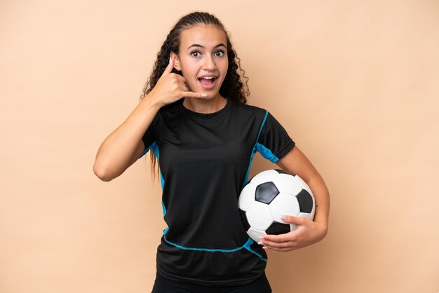 Mulher jovem jogador de futebol isolada em fundo bege fazendo gesto de telefone Ligue-me de volta sinal