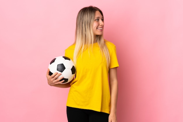 Mulher jovem jogador de futebol isolada em rosa olhando para o lado