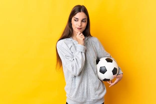 Mulher jovem jogador de futebol isolada na parede amarela, olhando para o lado e sorrindo
