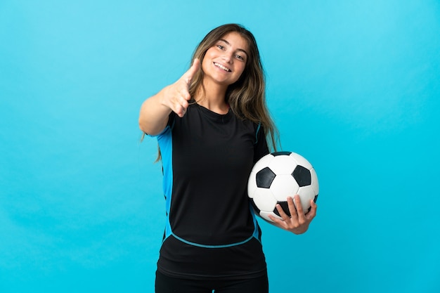 Mulher jovem jogador de futebol isolada na parede azul apertando as mãos para fechar um bom negócio