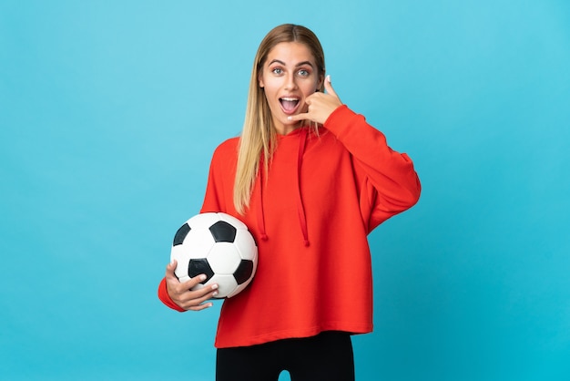 Mulher jovem jogador de futebol isolada na parede azul fazendo gesto de telefone. ligue-me de volta sinal