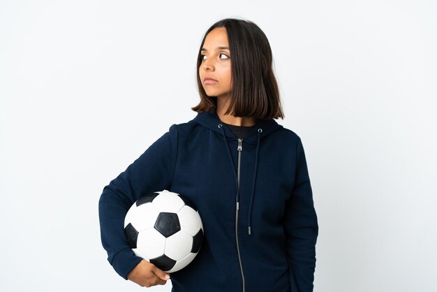 Mulher jovem jogador de futebol isolada na parede branca olhando para o lado