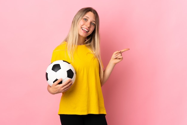 Mulher jovem jogador de futebol isolada na parede rosa apontando o dedo para o lado