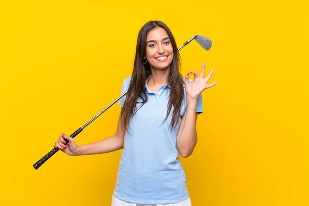 Mulher jovem jogador de golfe isolado parede amarela mostrando sinal ok com os dedos