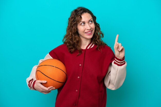 Mulher jovem jogadora de basquete caucasiana isolada em fundo azul apontando uma ótima ideia