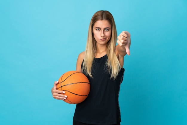 Mulher jovem jogando basquete em branco mostrando o polegar para baixo com expressão negativa