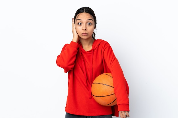 Mulher jovem jogando basquete em uma parede branca isolada frustrada e cobrindo os ouvidos