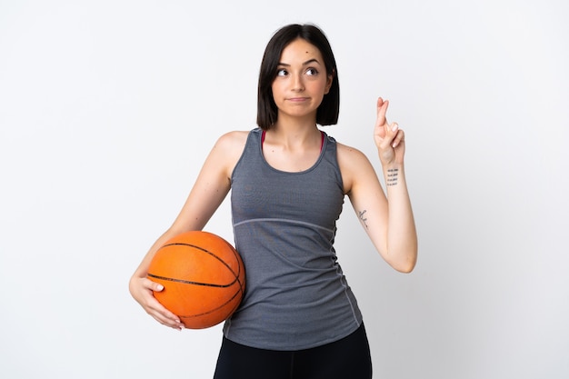 Mulher jovem jogando basquete isolada com os dedos cruzados e desejando o melhor