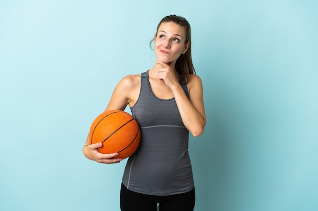 Mulher jovem jogando basquete isolada em uma parede azul e olhando para cima