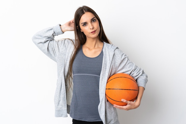 Mulher jovem jogando basquete isolada na parede branca com dúvidas
