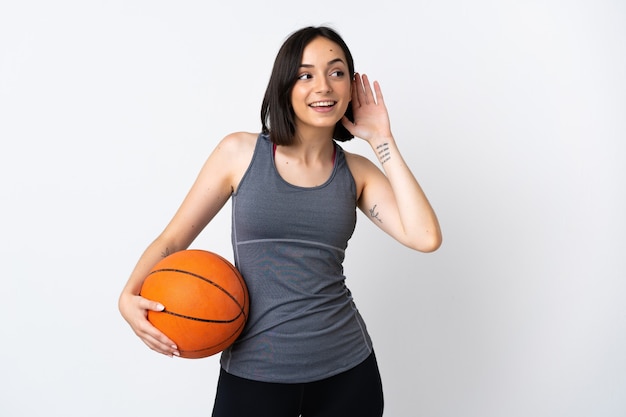 Mulher jovem jogando basquete, isolada no fundo branco, ouvindo algo colocando a mão na orelha