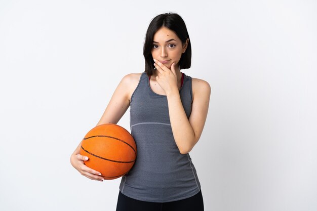 Mulher jovem jogando basquete isolada no fundo branco pensando