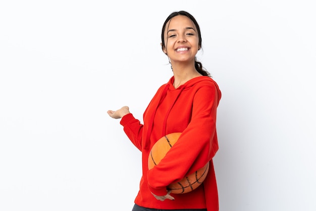 Mulher jovem jogando basquete isolado no branco estendendo as mãos para o lado para convidar para vir