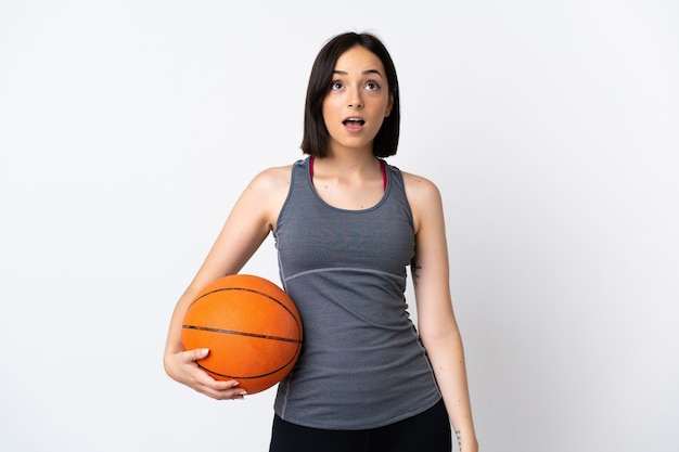 Mulher jovem jogando basquete isolado no branco, olhando para cima e com expressão de surpresa