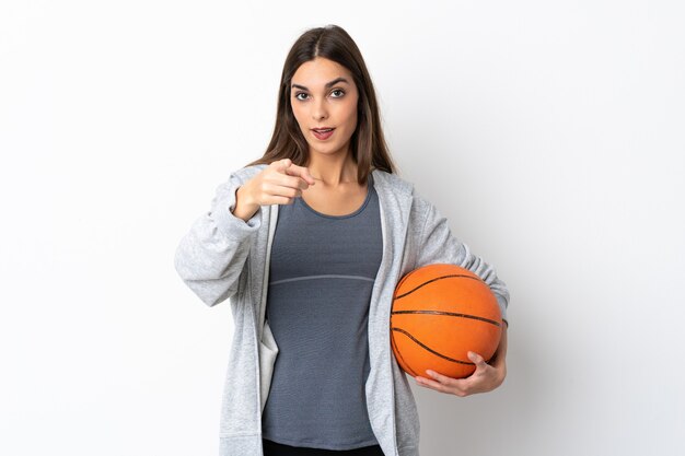 Mulher jovem jogando basquete isolado no branco surpresa e apontando para a frente