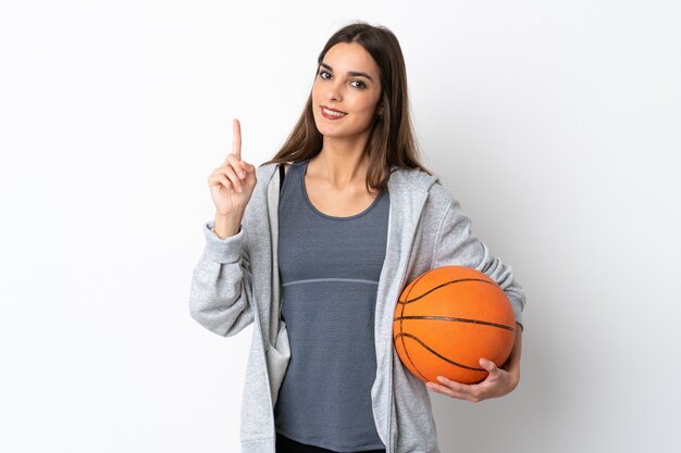 Mulher jovem jogando basquete isolado no fundo branco, mostrando e levantando um dedo em sinal dos melhores