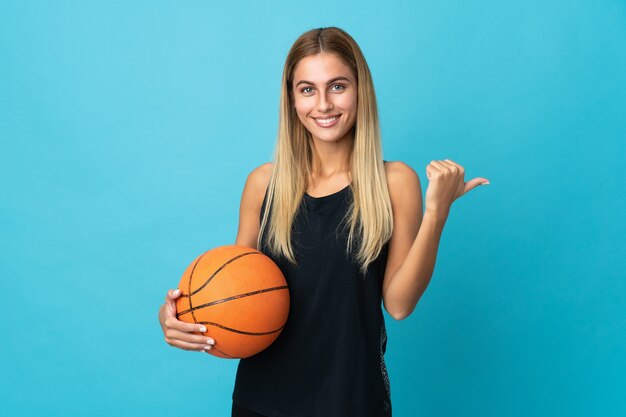 Mulher jovem jogando basquete posando isolada contra a parede em branco