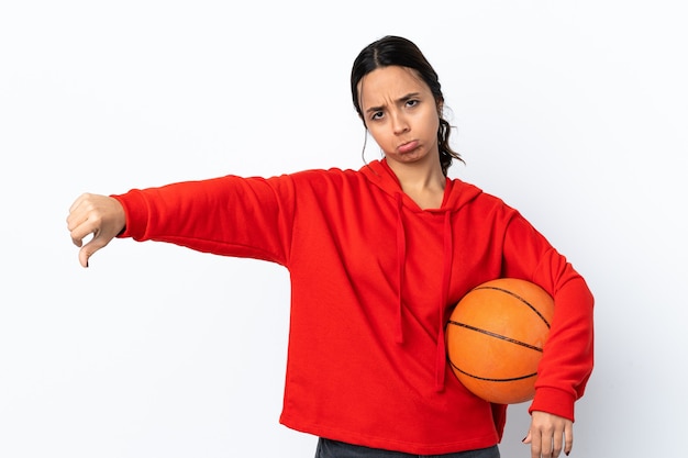 Mulher jovem jogando basquete sobre branco isolado, mostrando o polegar para baixo com expressão negativa