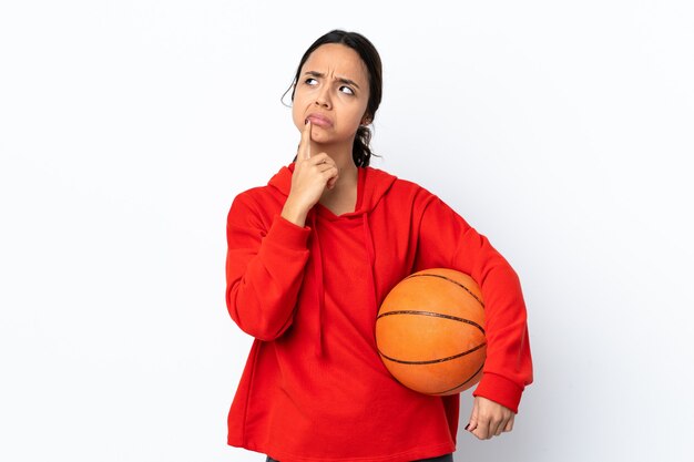 Mulher jovem jogando basquete sobre fundo branco isolado tendo dúvidas enquanto olha para cima