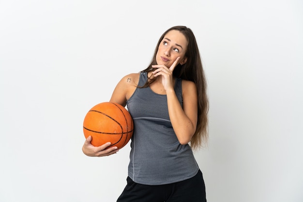 Mulher jovem jogando basquete sobre fundo branco isolado tendo dúvidas enquanto olha para cima